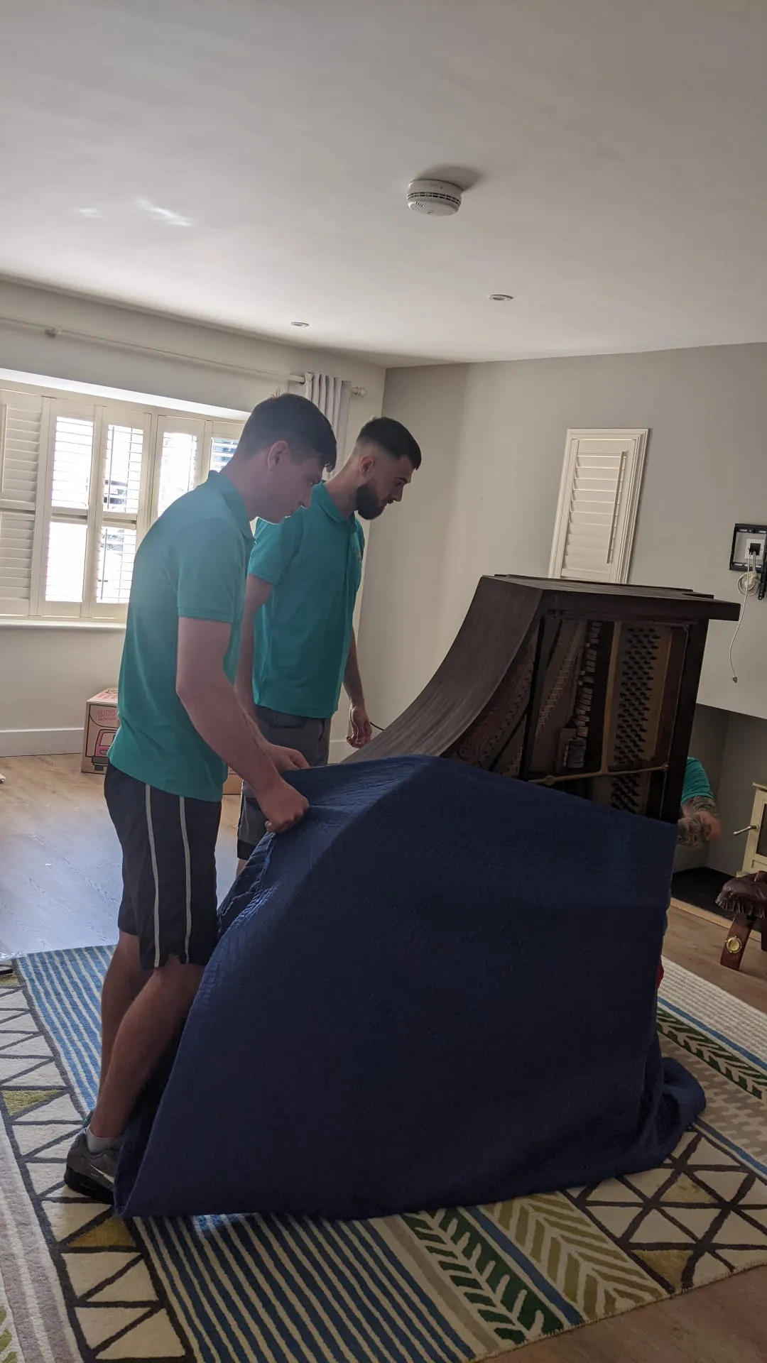 Two movers carrying an upright piano on a specialist piano dolly